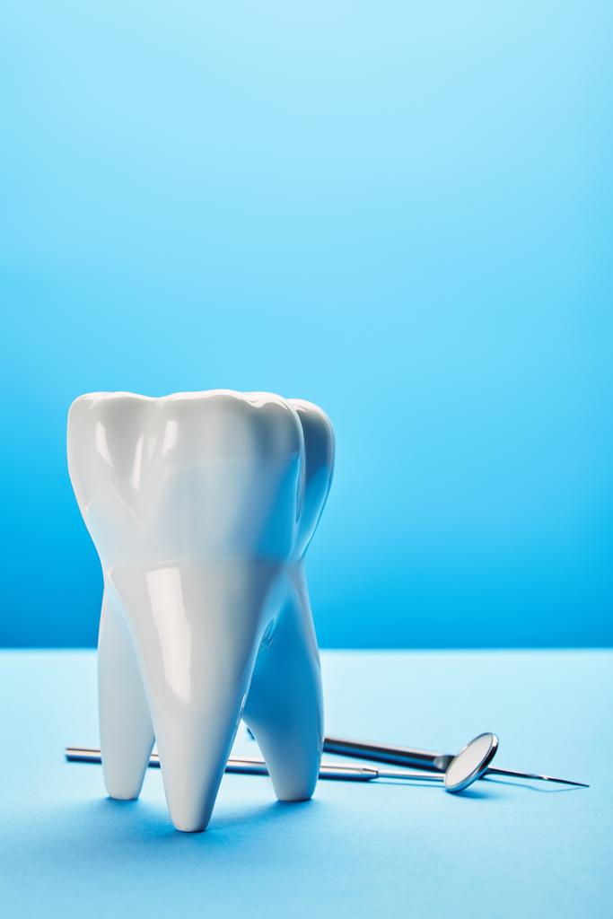 Close-up van steriele dentale spiegel, sonde en tand model gerangschikt op blauwe achtergrond - Foto, afbeelding