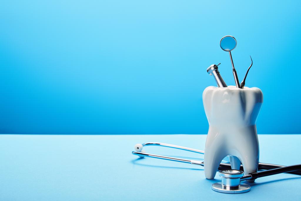vue rapprochée du modèle de dent blanche, du stéthoscope et des instruments dentaires en acier inoxydable sur fond bleu
 - Photo, image
