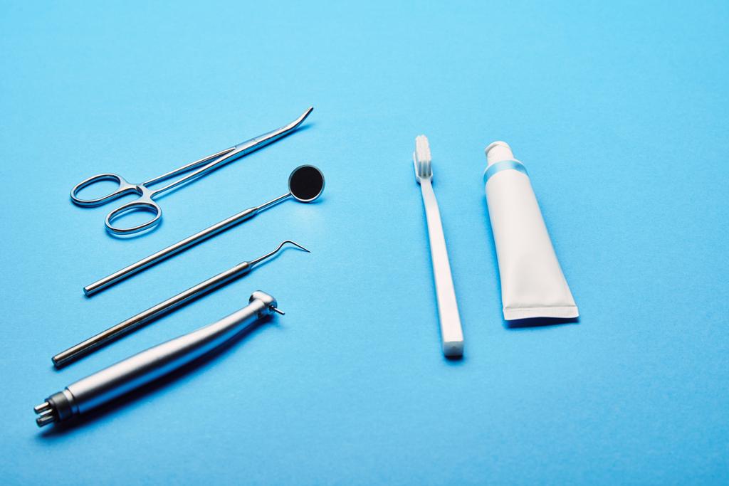 Close-up van regeling van steriele tandheelkundige instrumenten, stethoscoop, tandenborstel en tandpasta op blauwe achtergrond, tandheelkundige zorg concept - Foto, afbeelding