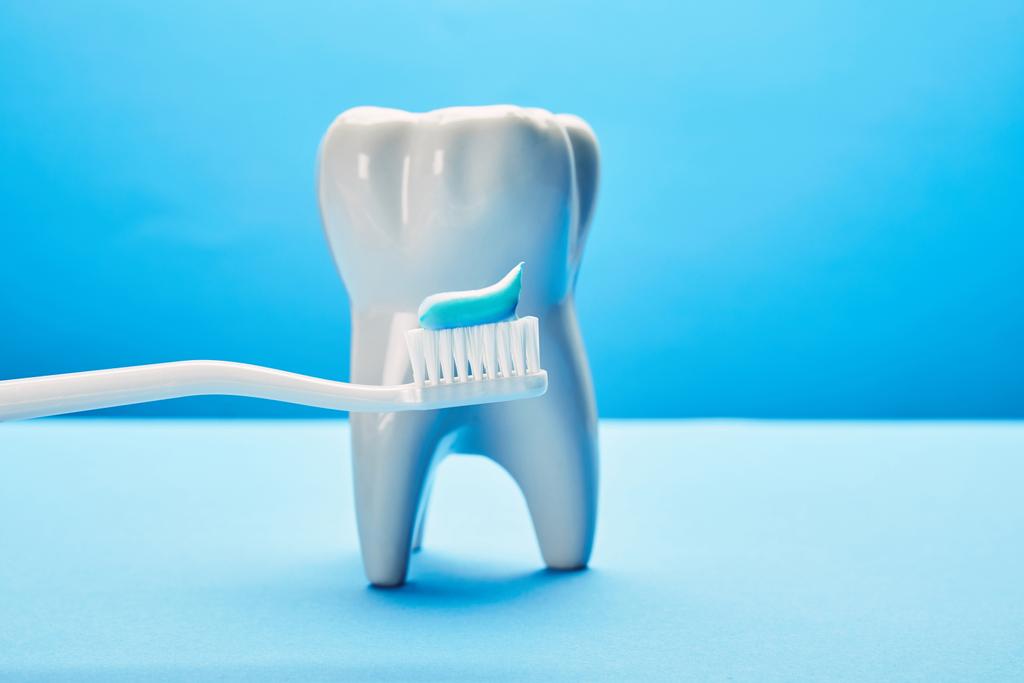 Close-up van model van de tand en tandenborstel met plakken op blauwe achtergrond, tandheelkundige zorg concept - Foto, afbeelding