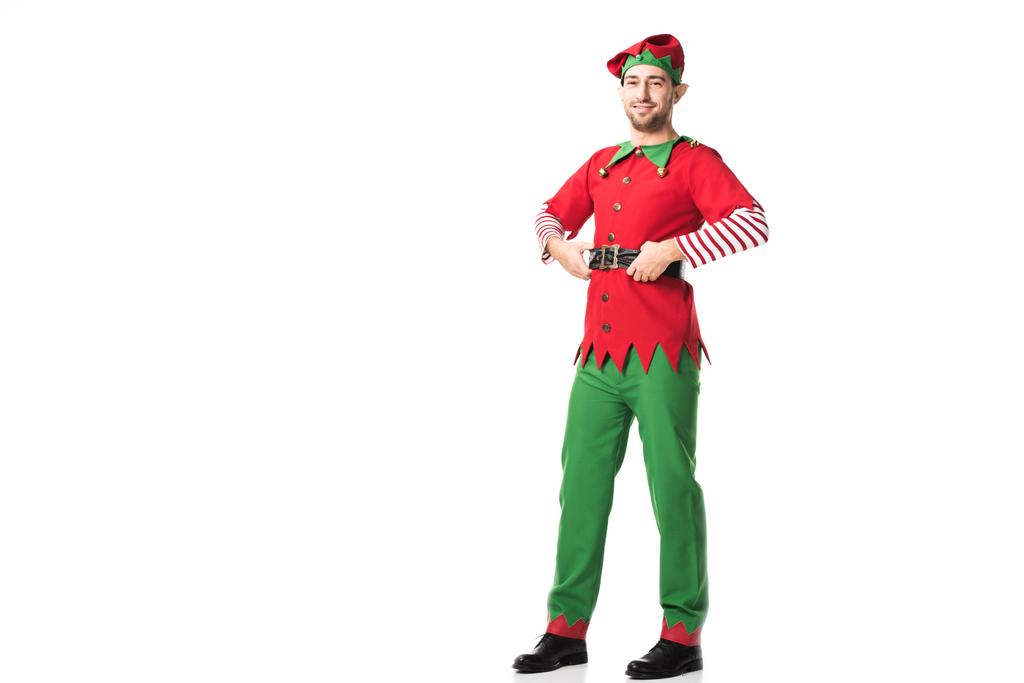 uśmiechnięty mężczyzna w Boże Narodzenie elf kostium patrząc na kamery z ręce na biodra na białym tle - Zdjęcie, obraz