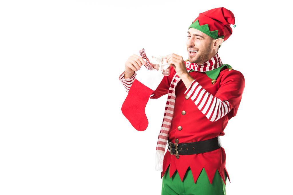 Mann im Weihnachtselfenkostüm schwingt Flügel und legt Geschenk in roten Weihnachtsstrumpf isoliert auf weiß - Foto, Bild