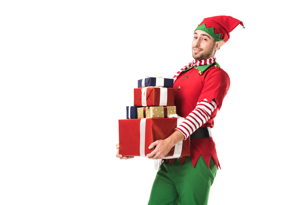 ο άνθρωπος στο κοστούμι elf Χριστούγεννα βλέπουν φωτογραφική μηχανή και να μεταφέρουν την σωρό δώρα που απομονώνονται σε λευκό - Φωτογραφία, εικόνα