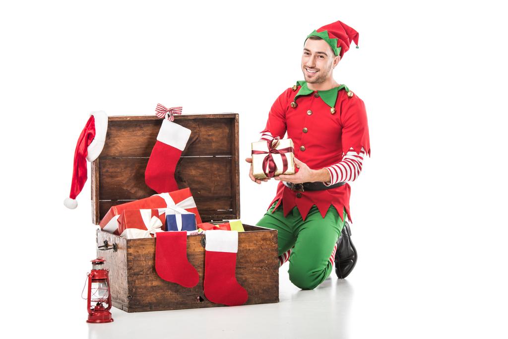 クリスマス エルフ衣装プレゼントの木製箱のそばに座って、ギフト白で隔離で笑みを浮かべて男 - 写真・画像