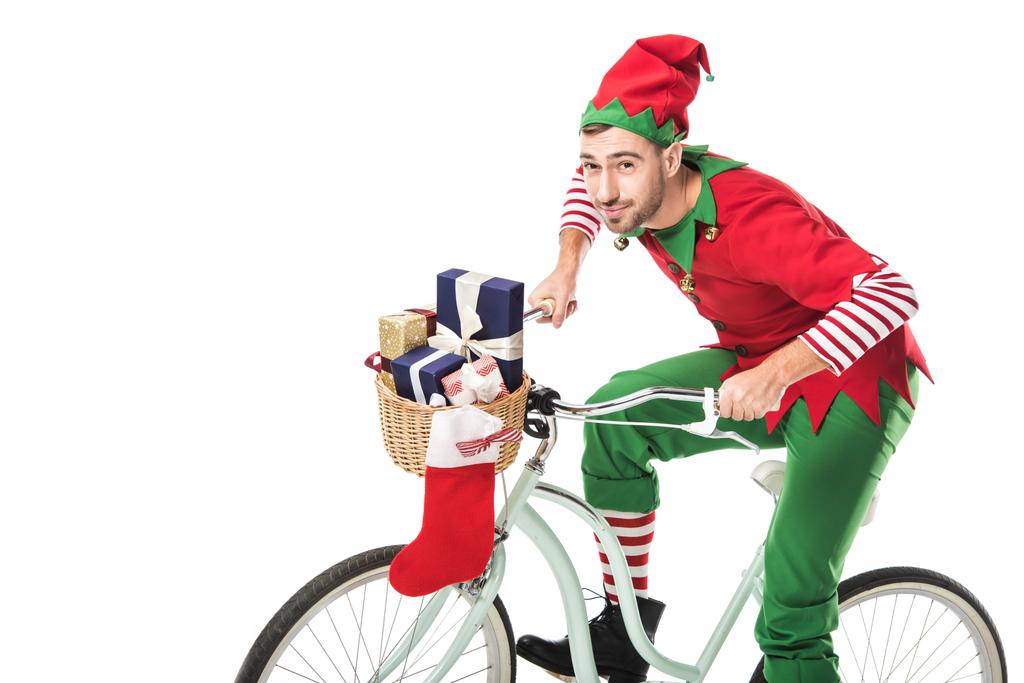 smiling man in christmas elf costume riding bike and transporting presents in basket isolated on white background - Photo, Image