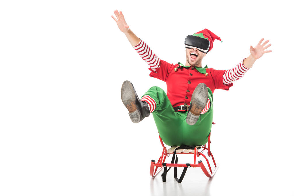 excited man in christmas elf costume riding sleigh and wearing virtual reality headset isolated on white - Photo, Image