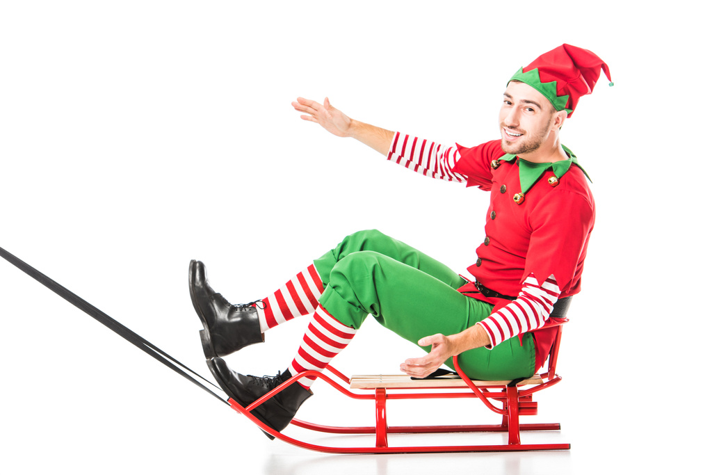 animado feliz homem no Natal elfo traje equitação trenó e olhando para câmera isolada no branco
 - Foto, Imagem