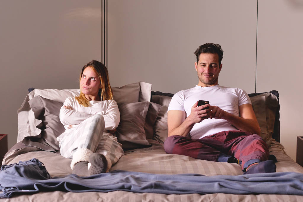 Aviopari sängyssä käyttää puhelinta erikseen viestien lähettämiseen tai sosiaalisten verkostojen käyttämiseen eikä enää puhu toisilleen. Käsite: uudet sukupolvet, erottaminen, teknologia
. - Valokuva, kuva