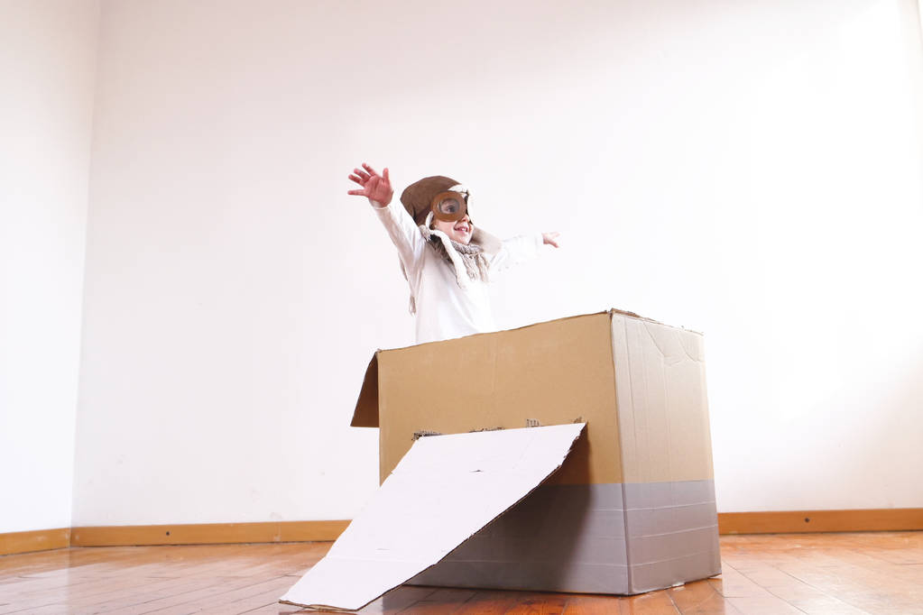 Gelukkig schattig meisje, gekleed als pilot spelen in handgemaakte kartonnen doos vliegtuig  - Foto, afbeelding