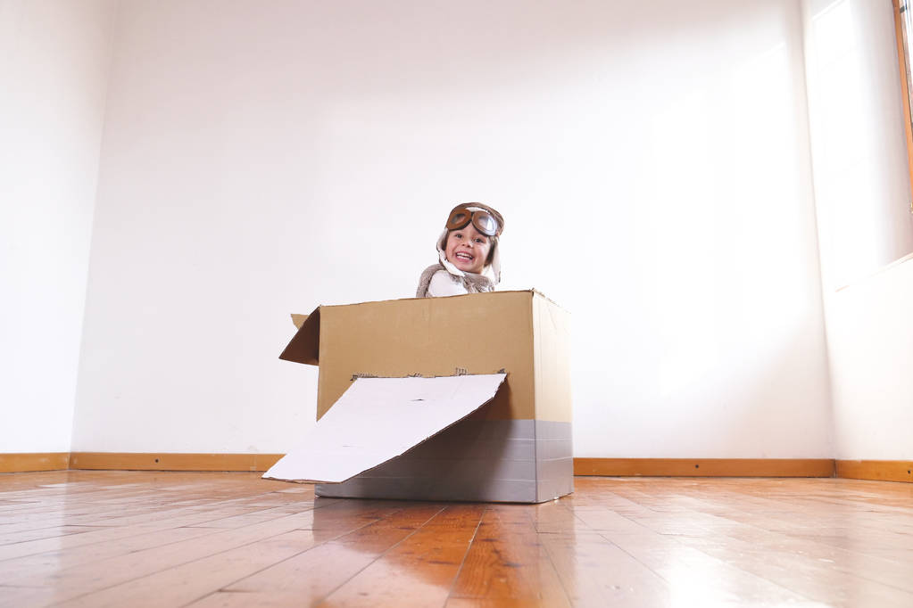 sorridente adorabile bambina vestita da pilota che gioca in cartone fatto a mano aereo scatola
  - Foto, immagini