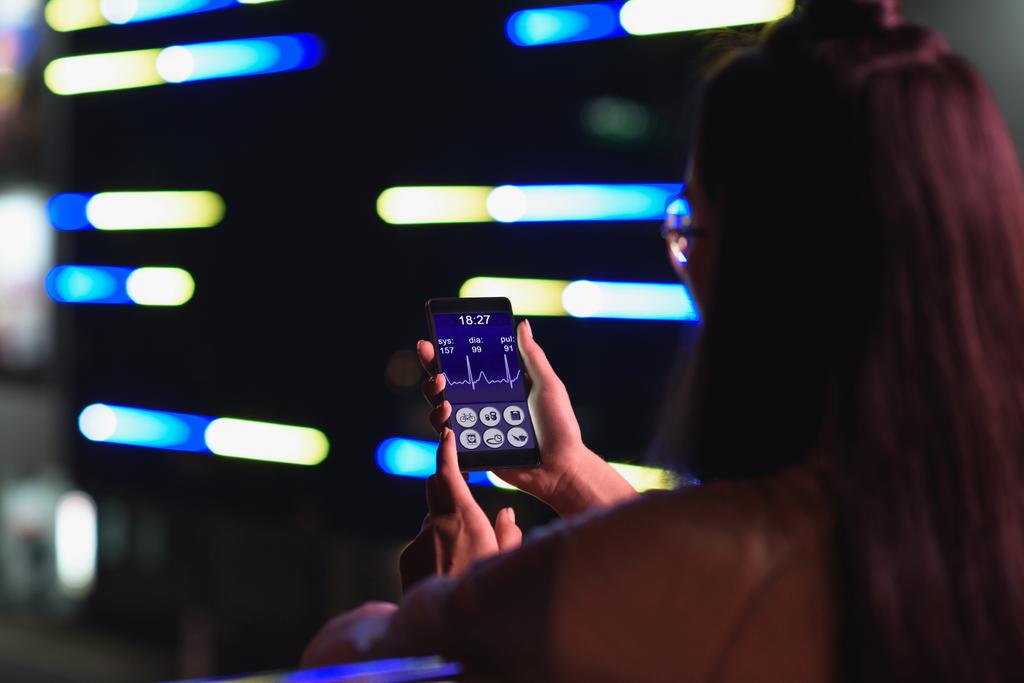 visão traseira da menina segurando smartphone com aparelho médico na rua com luz de néon à noite, cidade do conceito futuro
 - Foto, Imagem