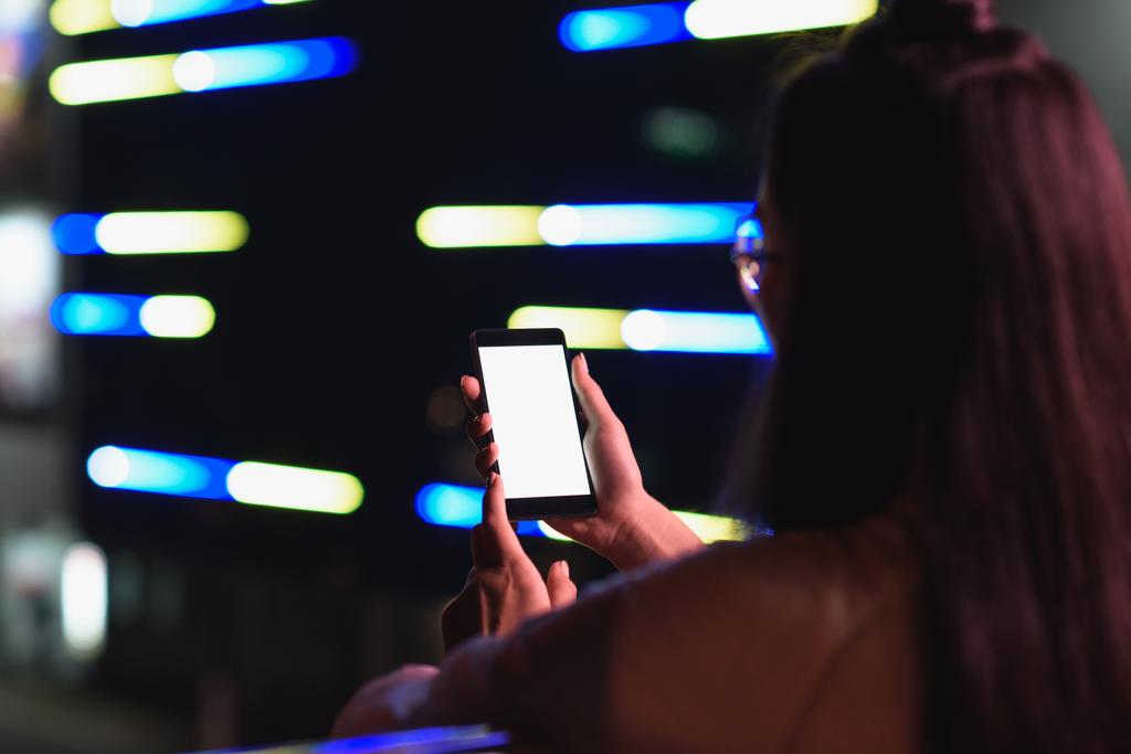 arkadan görünüşü akşamlar, gelecekteki kavramının şehir smartphone ile boş bir beyaz ekran ile neon ışık Caddesi üzerinde tutan kız - Fotoğraf, Görsel