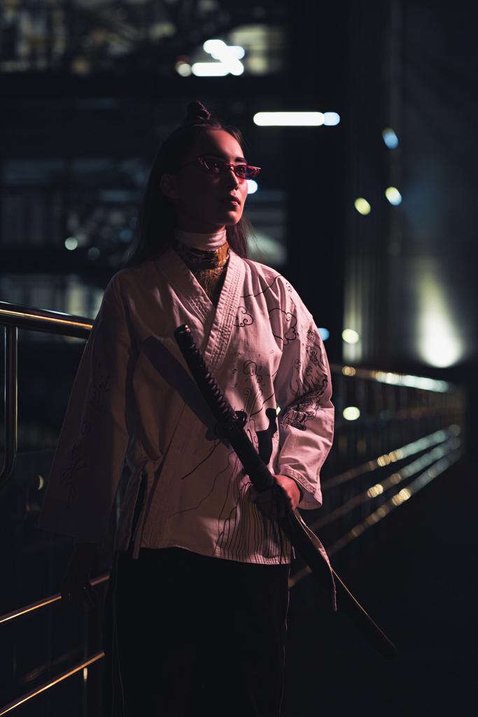 atractivo asiático chica en blanco kimono holding katana en calle con neón luz en la noche, ciudad de futuro concepto
 - Foto, imagen