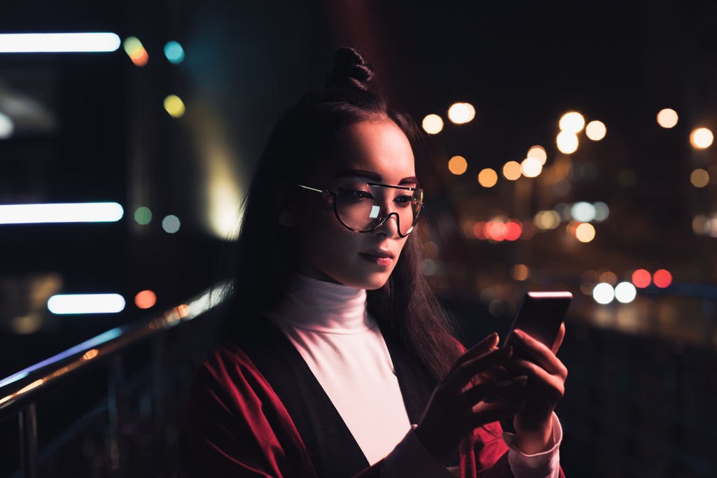 atraktivní asian girl v burgundské kimono a brýle pomocí smartphone na ulici s neon světlo v večer, město budoucí koncepce - Fotografie, Obrázek