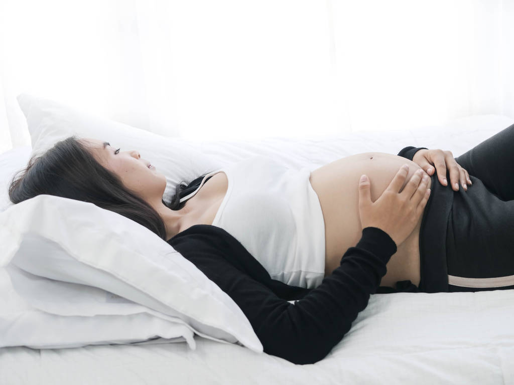 Asiatische Schwangere, die zu Hause im Bett liegt, Lifestyle-Konzept. - Foto, Bild