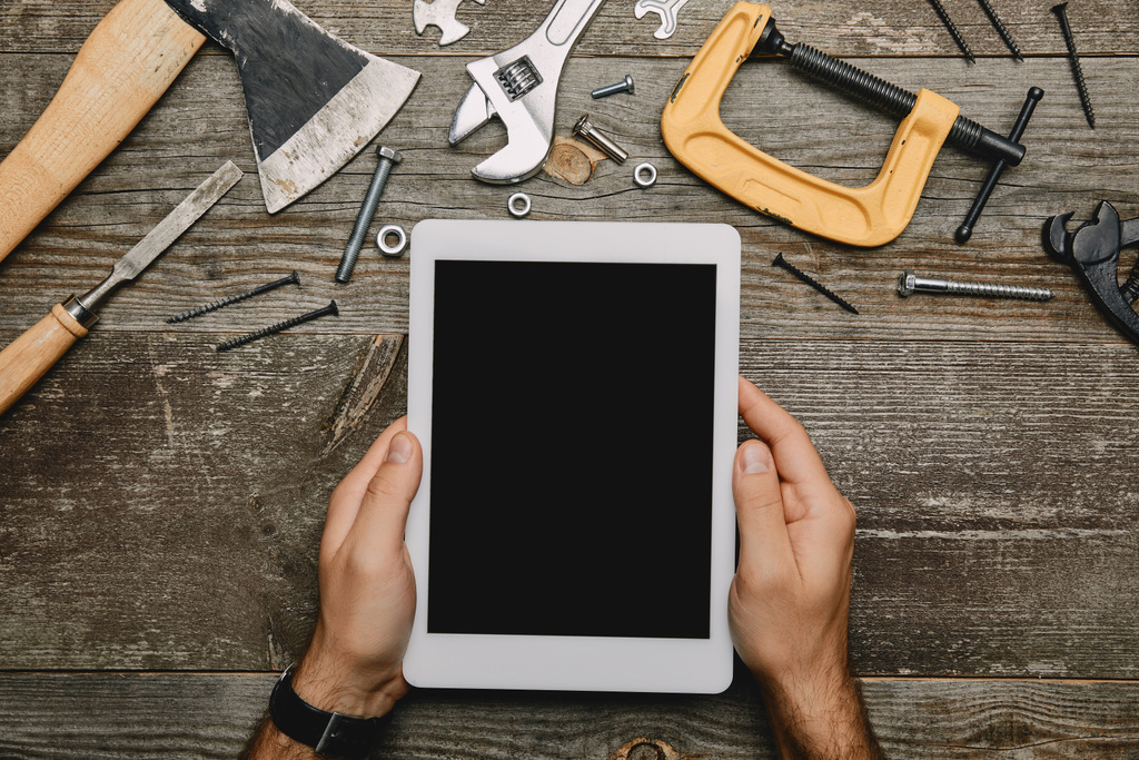 Teilansicht des Arbeiters mit digitalem Tablet in der Werkstatt mit verschiedenen Tischlerwerkzeugen  - Foto, Bild