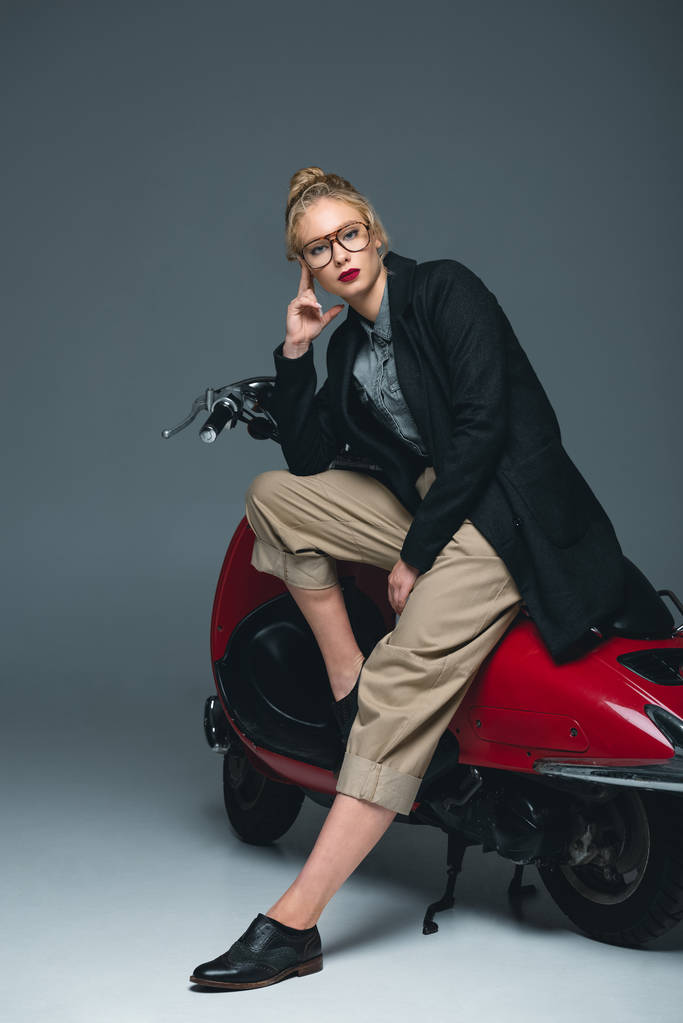 atractiva mujer joven de moda posando en scooter rojo en gris
 - Foto, Imagen