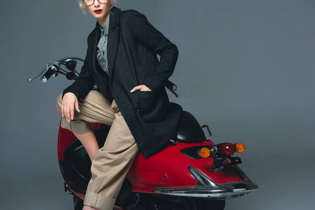 vue recadrée de fille à la mode posant sur scooter rouge isolé sur gris
 - Photo, image