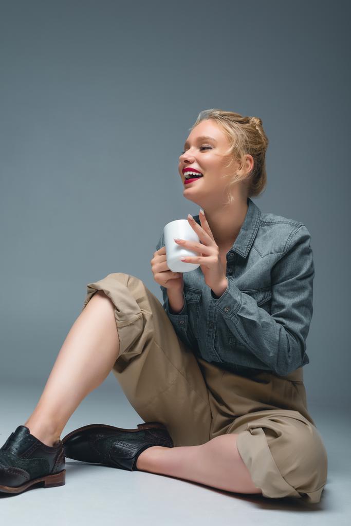 atrakcyjne stylowe śmiejąca się dziewczyna z herbatę, siedząc na szary - Zdjęcie, obraz