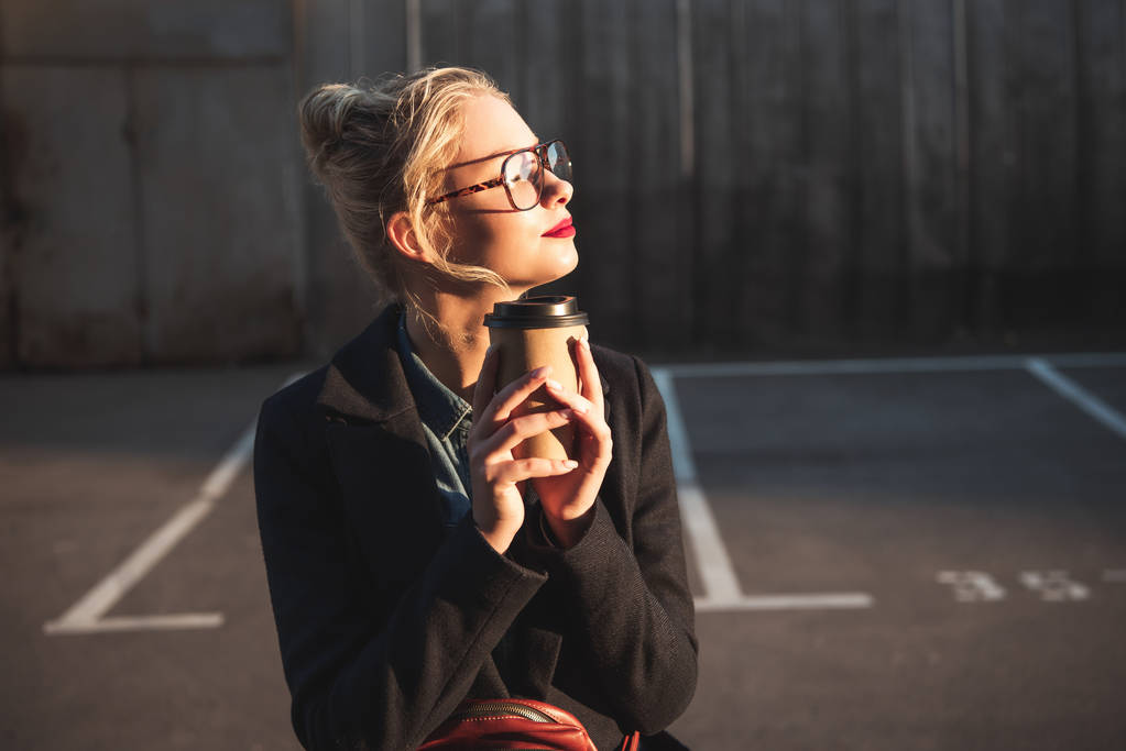 stylish dreamy girl holding paper cup of coffee on parking - Photo, Image