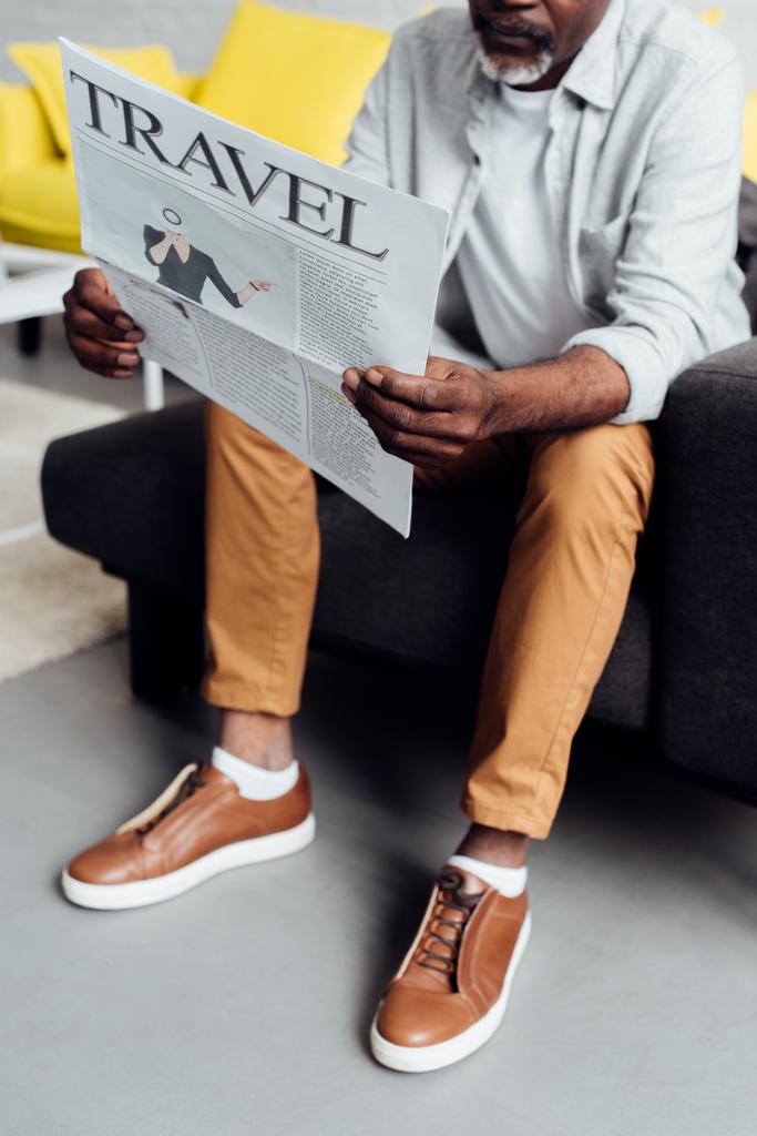 Afryki amerykański człowiek siedzi na kanapie i czytanie gazety podróży  - Zdjęcie, obraz