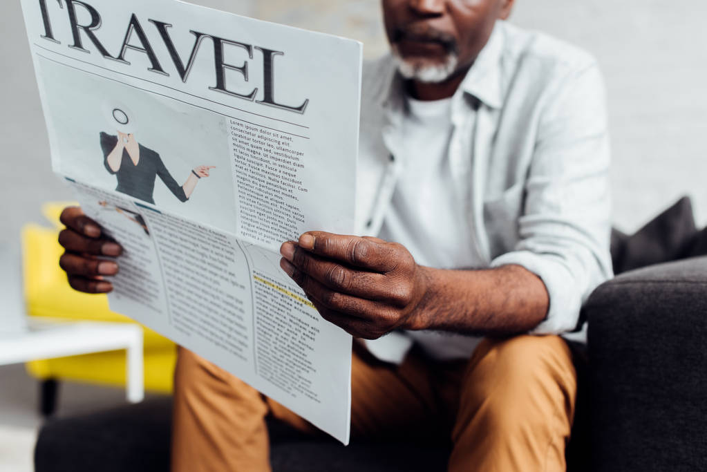 lähikuva afrikkalainen amerikkalainen mies istuu sohvalla ja lukeminen matkustaa sanomalehti
  - Valokuva, kuva
