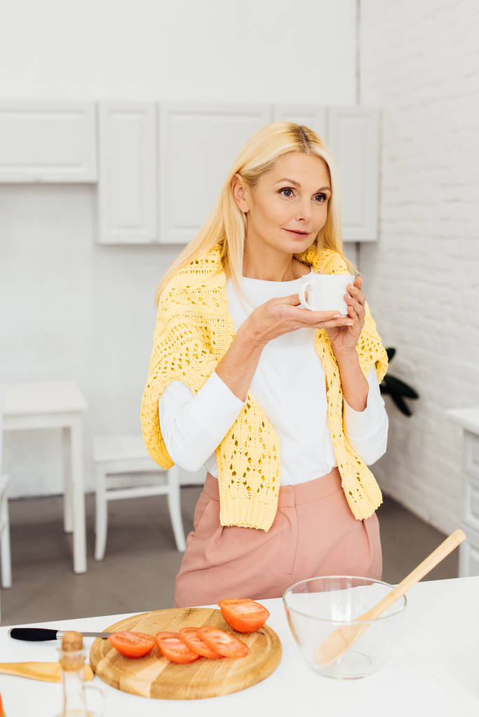 красива жінка стоїть з чашкою кави на кухні
 - Фото, зображення