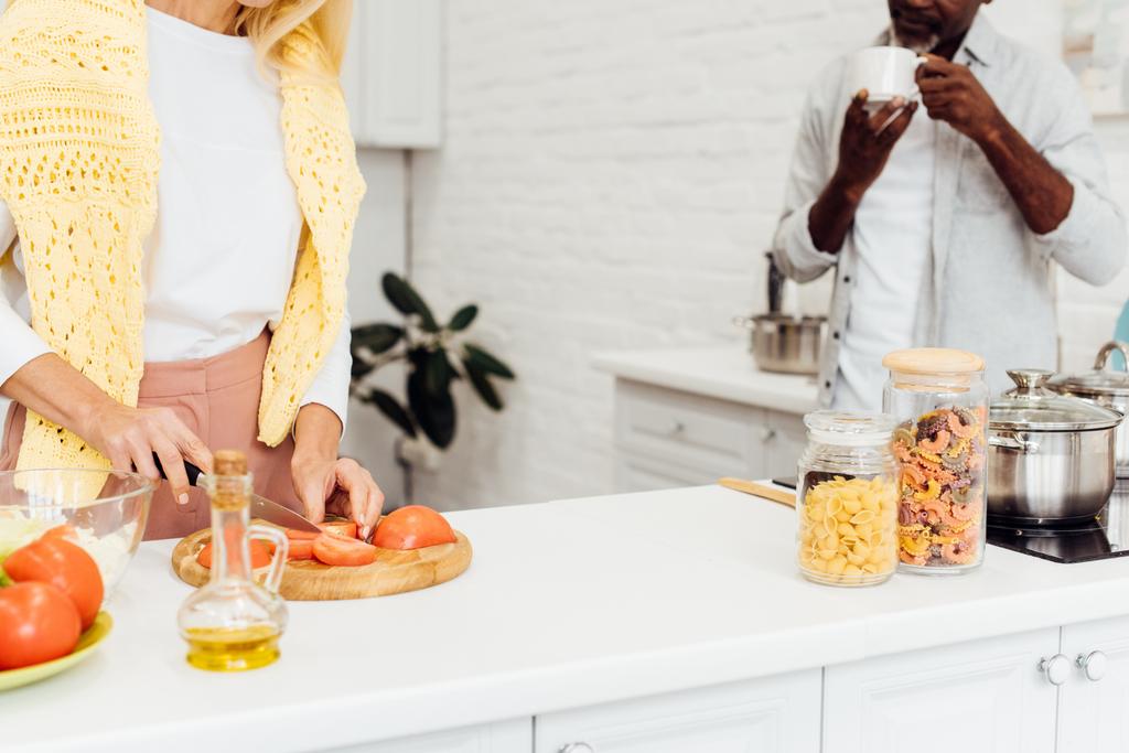 rajattu näkymä kypsä blondi nainen ruoanlaitto illallinen kun afrikkalainen amerikkalainen mies juo kahvia
 - Valokuva, kuva
