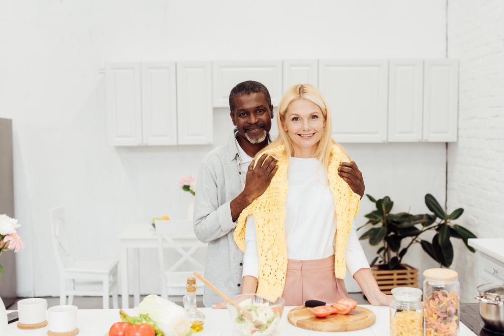 Lächelndes Paar kocht Abendessen und umarmt sich in Küche - Foto, Bild
