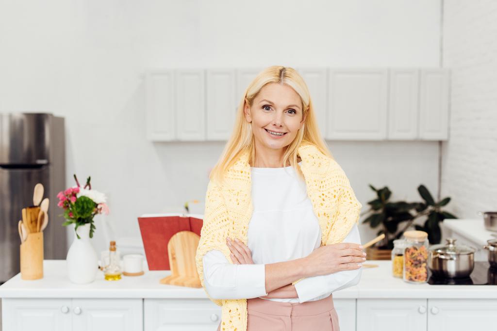 sorridente donna bionda con le braccia incrociate in piedi in cucina
 - Foto, immagini