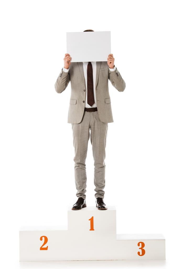 επιχειρηματίας που κρύβεται πίσω από μια κενή κάρτα, ενώ στέκεται στο βάθρο νικητών απομονωθεί σε λευκό - Φωτογραφία, εικόνα