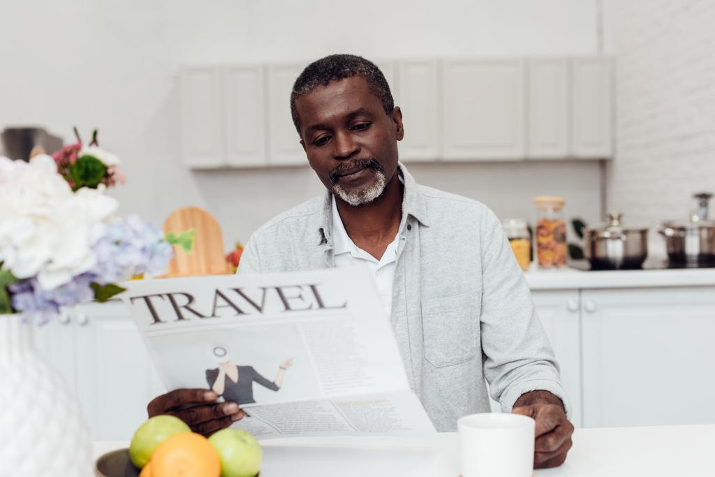 homem americano africano sentado à mesa e lendo jornal de viagem na cozinha
 - Foto, Imagem