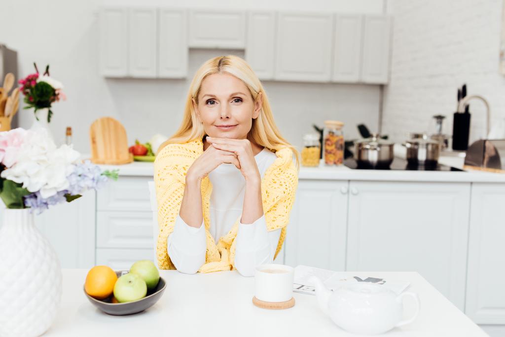 mujer sonriente sentada en la cocina y tomando té por la mañana
 - Foto, Imagen