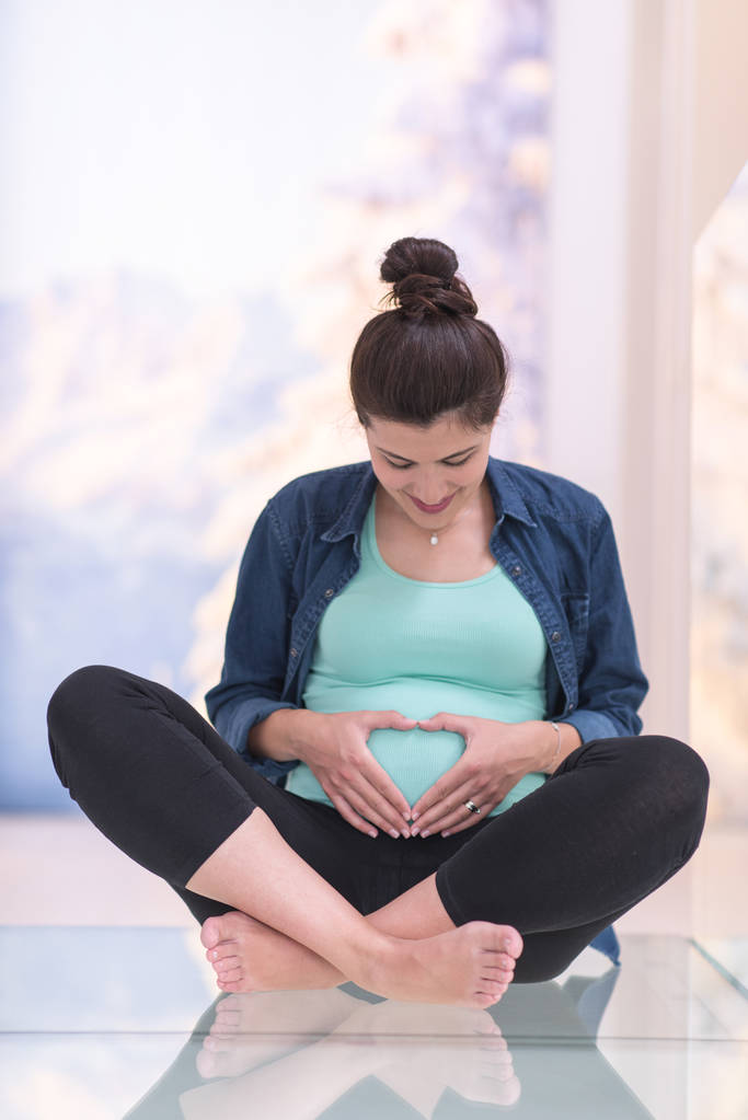 ευτυχισμένος έγκυες γυναίκες απολαμβάνουν εγκυμοσύνη χαλαρώνοντας στο σπίτι κάθεται στο πάτωμα - Φωτογραφία, εικόνα