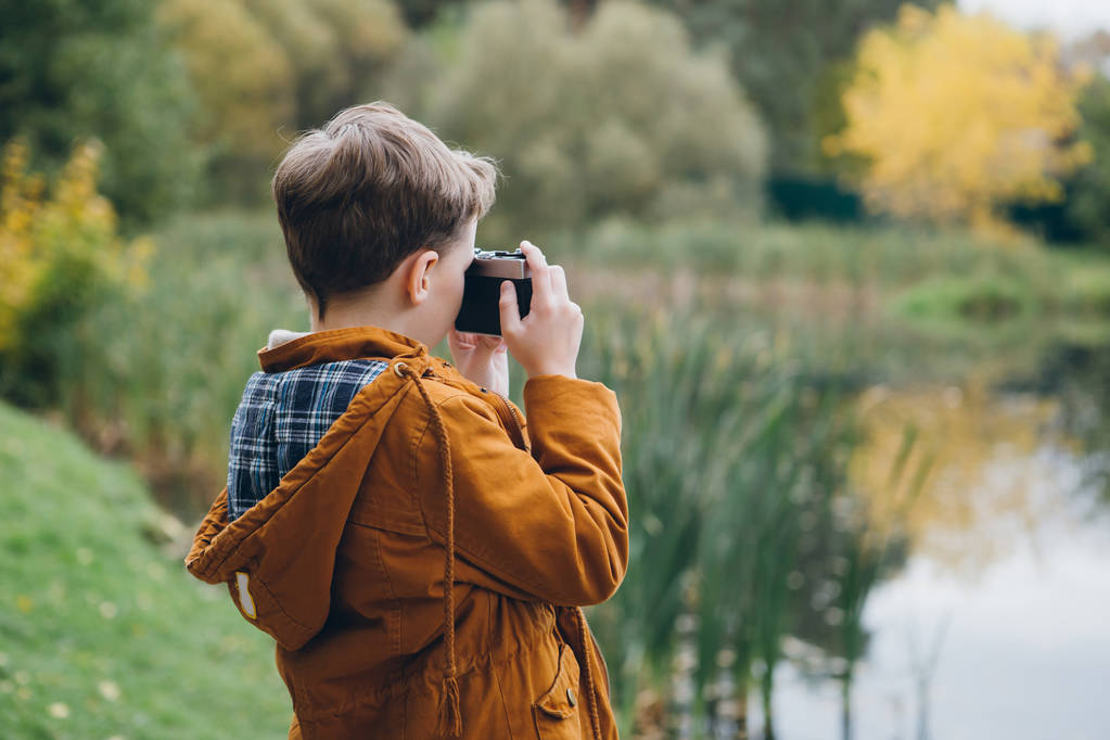 Aranyos fiú sétál, és színes őszi Park jelent. A fiú a kamera veszi a képek. Alakformálás. - Fotó, kép