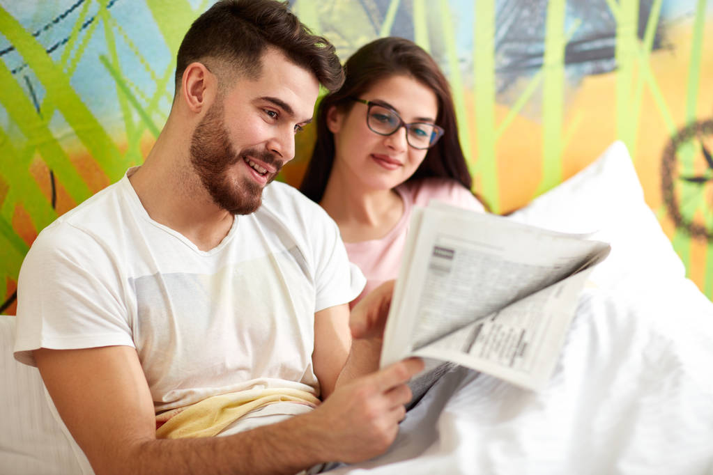 A fiatal pár olvasó újság együtt az ágyban reggel  - Fotó, kép