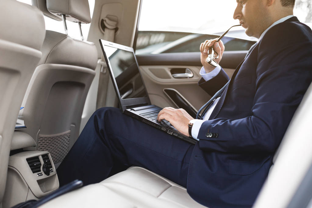 un giovane uomo d'affari in giacca e cravatta è seduto sul sedile posteriore di un'auto d'affari con un computer portatile e un notebook, trattative commerciali
 - Foto, immagini