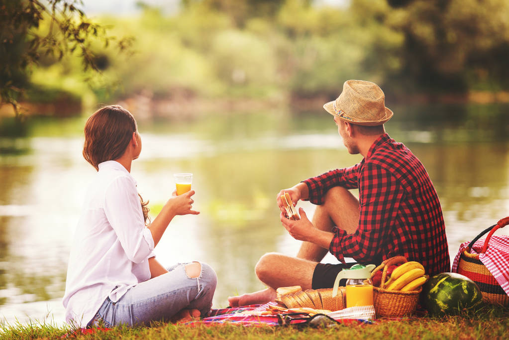 Couple amoureux profiter du temps de pique-nique boire et manger dans la belle nature sur la rive de la rivière
 - Photo, image