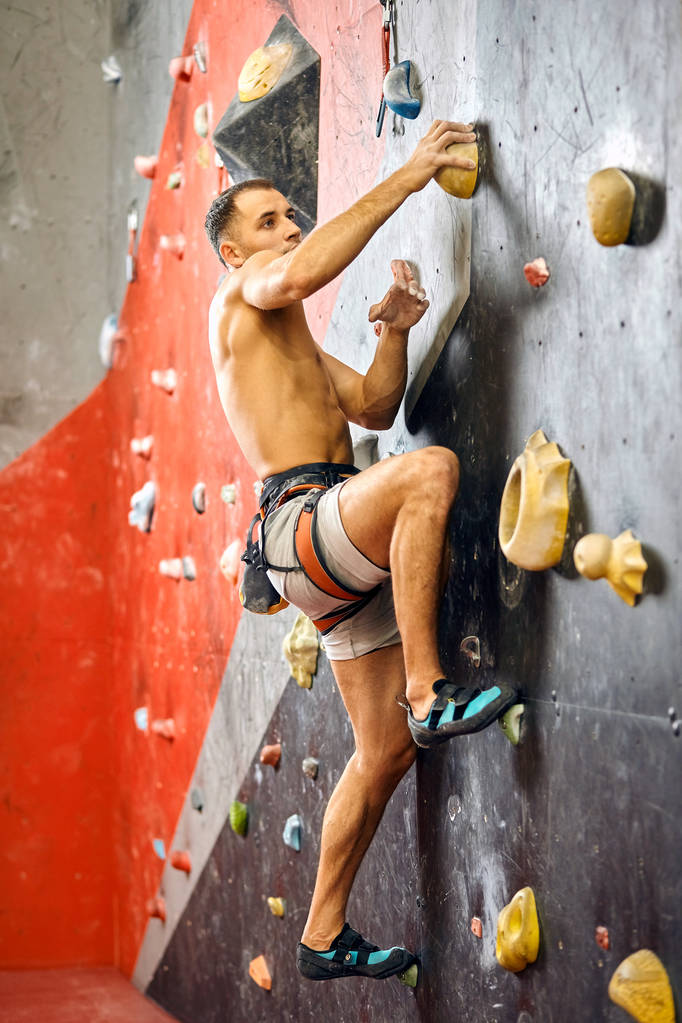 Homme grimpeur faisant de l'exercice dans la salle de gym, grimpant sur un mur artificiel avec des rochers. - Photo, image