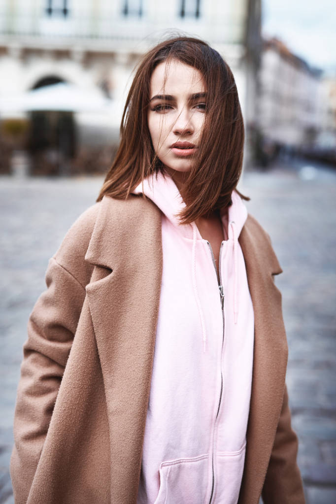jovem mulher de casaco marrom e rosa com capuz posando na rua
 - Foto, Imagem