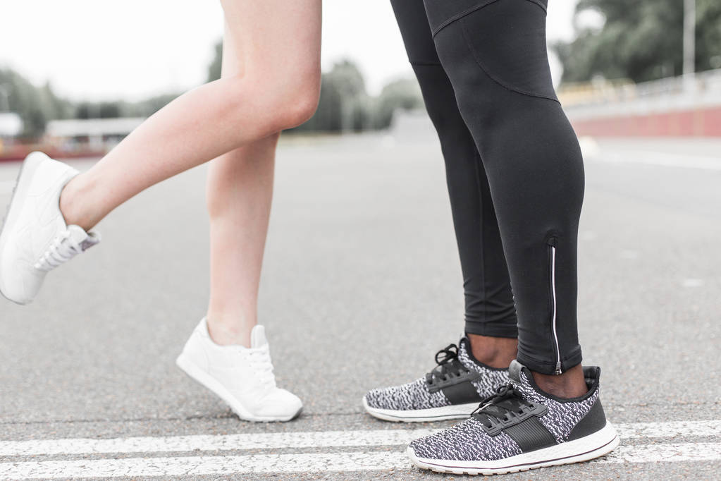 Love sport concept - running couple kissing. Closeup of running shoes and girl standing on toes to kiss boyfriend during jogging workout training outdoors - Photo, Image