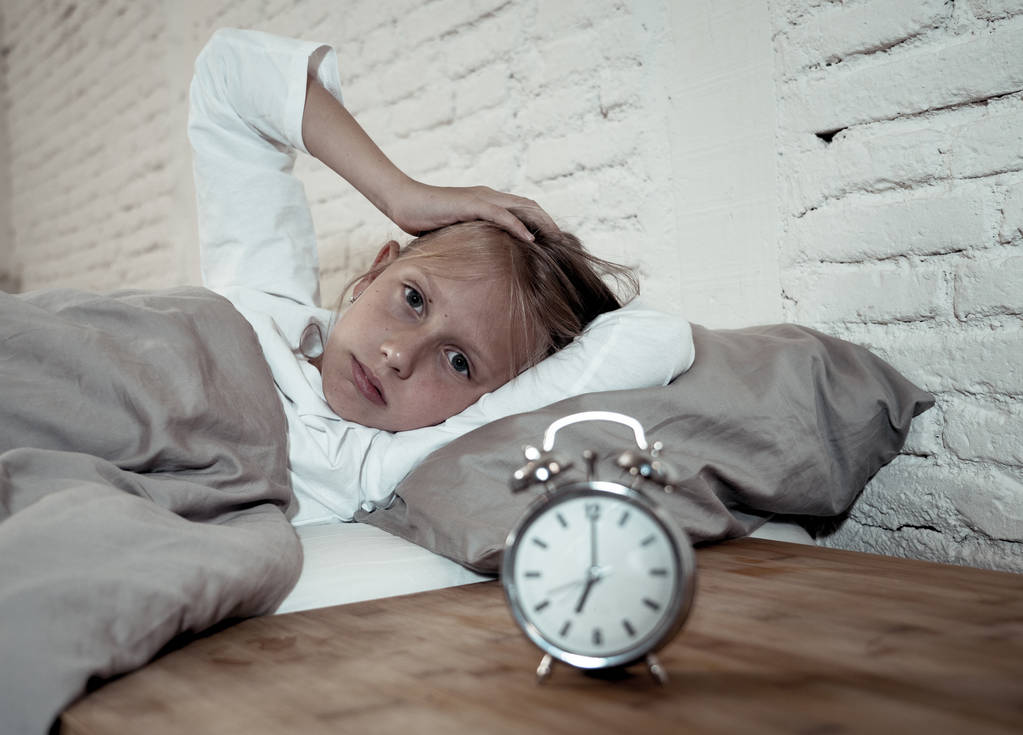 Słodkie bezsennych dziewczynki leżącego smutny w łóżku patrząc na budzik, mających się obudzić, ale uczucie zmęczenia bezsennych w kłopotach pobyt snu zaburzenia snu lęki nocne i koncepcja bezsenność dzieci. - Zdjęcie, obraz