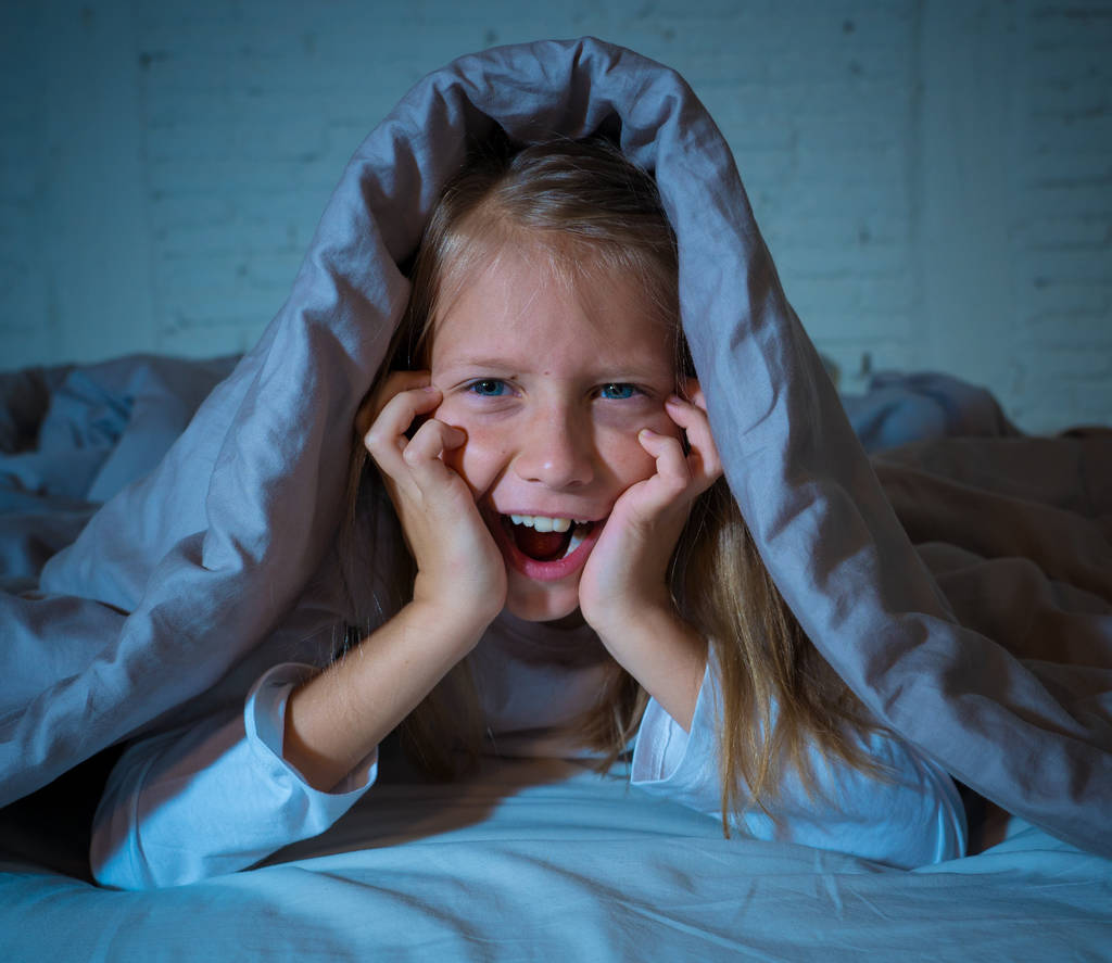 Cute asleep girl screaming and crying after frightening or upsetting dream covering herself with blanket in bed at night in mood dramatic lighting in Sleep terrors Nightmares and Sleeping disorders. - Photo, Image