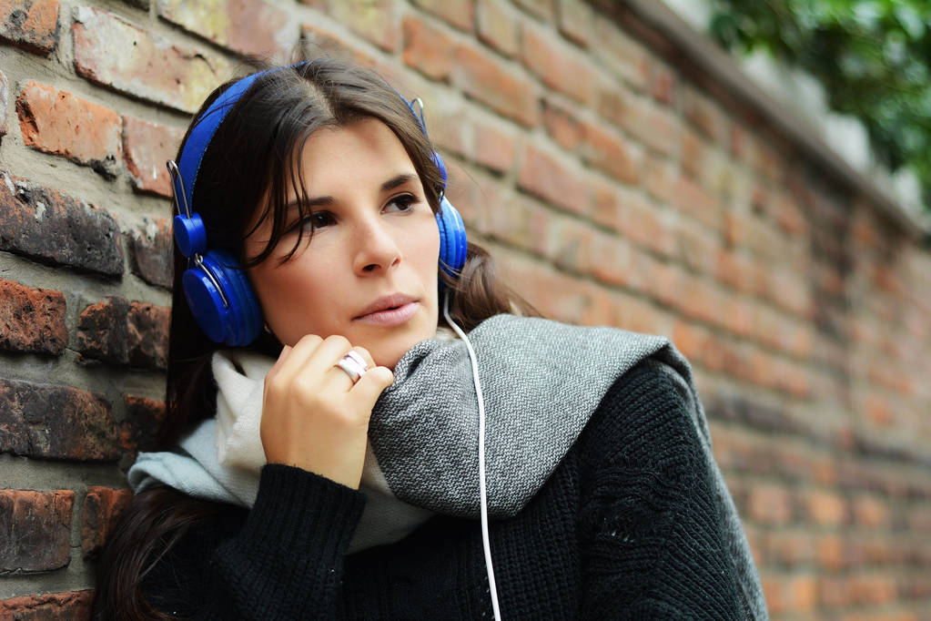 Portrait of young latin woman with blue headphones against a wall. - Photo, Image