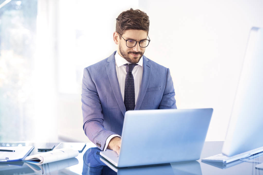 Tiro de jovem empresário vestindo terno enquanto sentado na frente do laptop e trabalhando em projeto de negócios. - Foto, Imagem