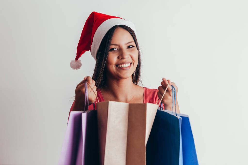 junge Frau mit Weihnachtsmütze mit Einkaufstaschen auf weißem Hintergrund - Foto, Bild