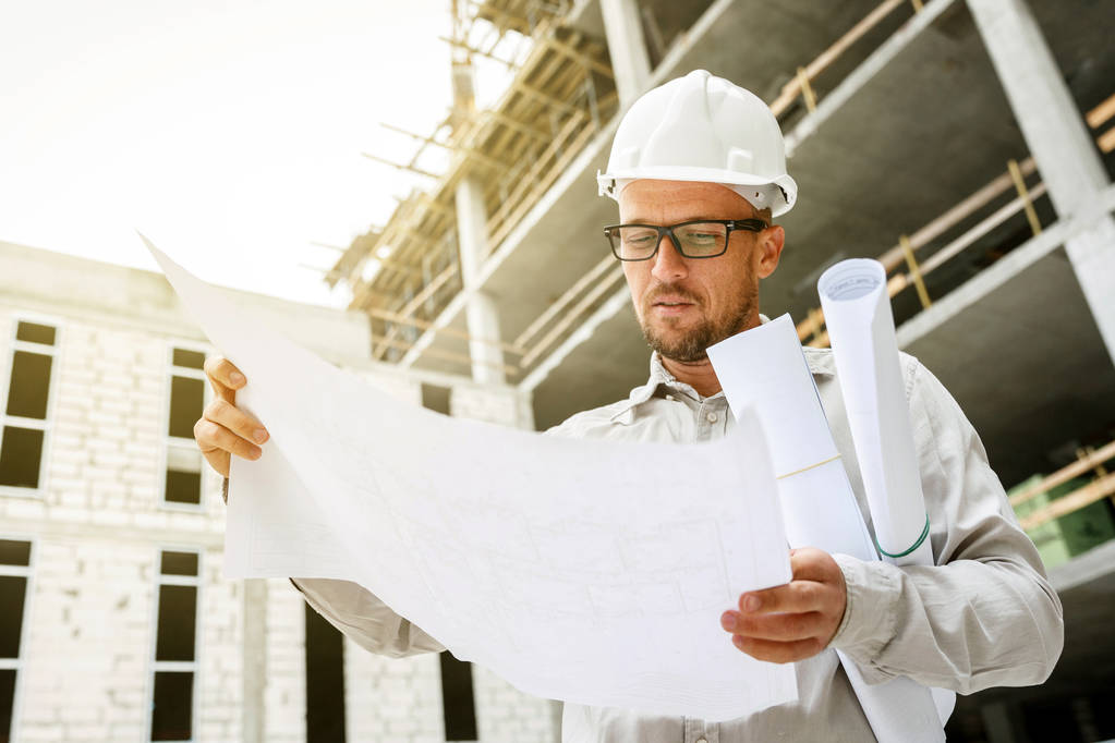Ingeniero de construcción en un sombrero blanco inspeccionando planos en un sitio de construcción. Desarrollo y concepto de industria de la construcción
 - Foto, imagen
