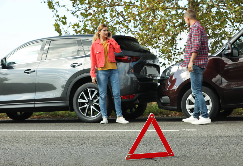 Hätäpysäytysmerkki lähellä ihmisiä, jotka keskustelevat auto-onnettomuudesta tiellä. Autovakuutus
 - Valokuva, kuva