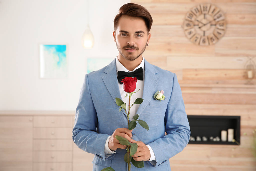 Handsome man in formal wear holding red rose indoors - Valokuva, kuva