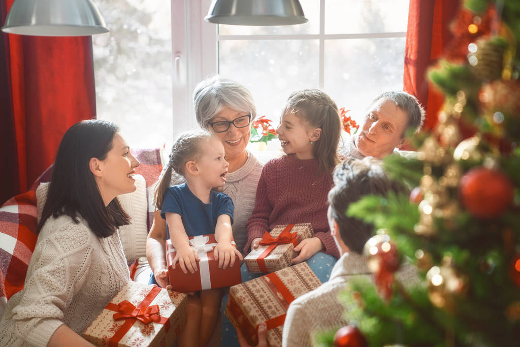 Joyeux Noël et Joyeuses Fêtes ! Grand-mère, grand-père, maman, père et enfant échangeant des cadeaux. Parents et fille s'amusent près d'un arbre à l'intérieur. Famille aimante avec des cadeaux dans la chambre
. - Photo, image